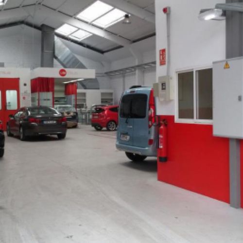 Vista del taller con puerta de oficina en primer plano y nave con coches y cabina de pintura al fondo