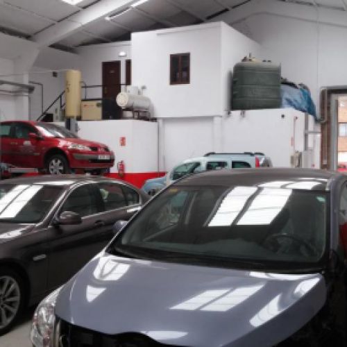 Interior del taller con coches aparcados y puerta de entrada abierta al fondo