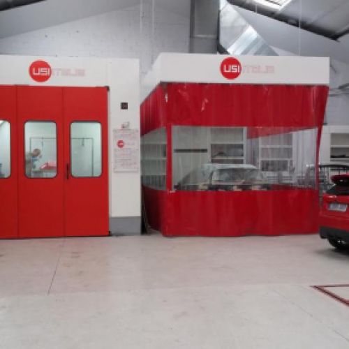 Imagen en primer plano de cabinas de pintura con lona y puerta en color rojo y coches aparcados a los lados