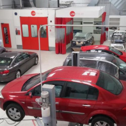 Vista del interior del taller con coches elevados en reparación y puerta roja de cabina de pintura