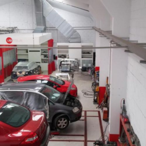 Interior del taller grande con cabina de pintura a la izquierda y coches en reparación a la derecha